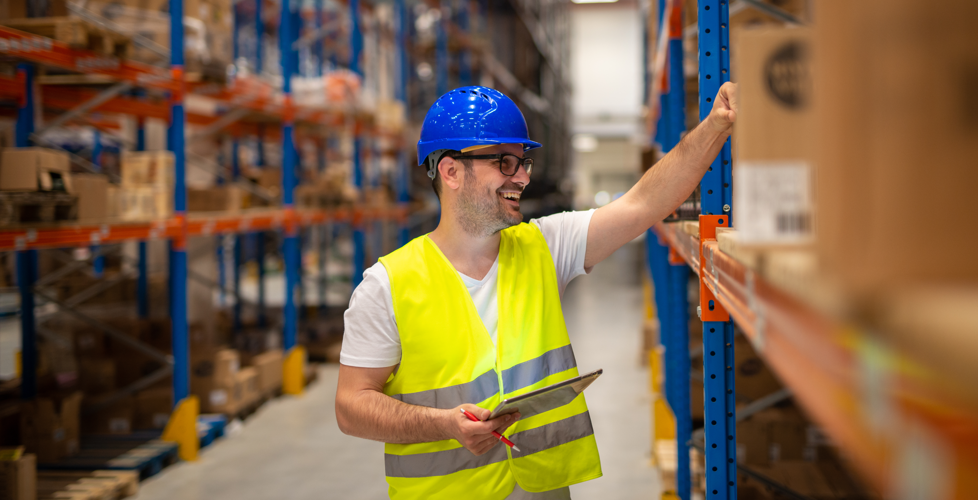 Manufacturing and distribution employee holds and clipboard and smiles while checking a stock shelf.